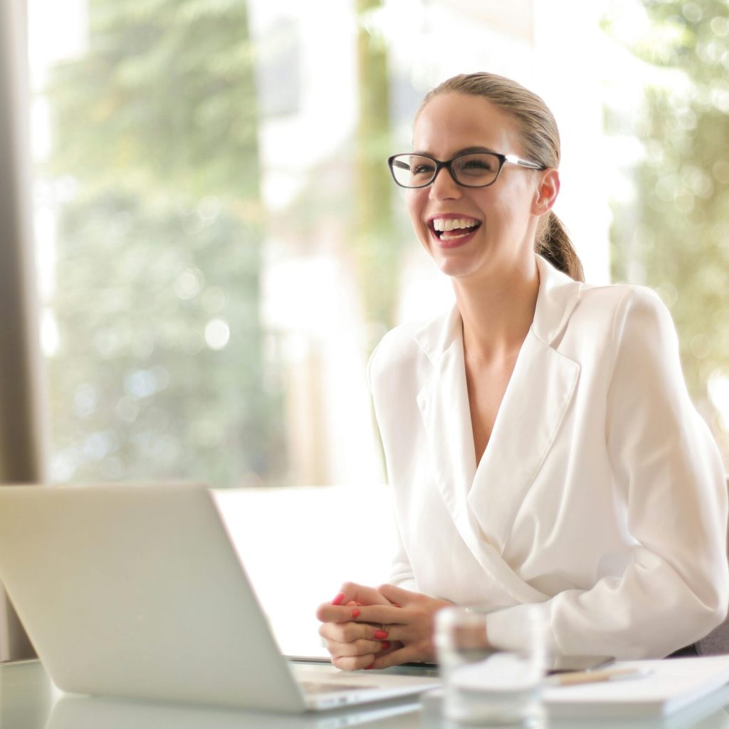 pexels-photo-3756679-3756679 Cheerful businesswoman in glasses working on a laptop, in a bright and modern office setting.